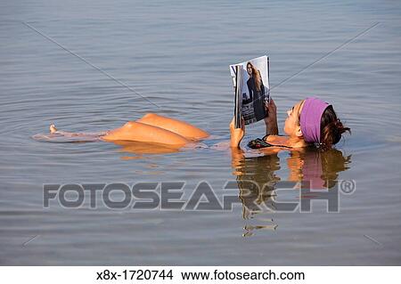 Picture - Young woman floating and reading a magazine in the dead sea, Jordan. Fotosearch