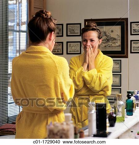 Stock Image - young woman giggling in front of bathroom mirror. Fotosearch