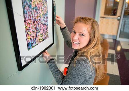 Young woman hanging photographs on wall. View Large Photo Image Stock Image - Young woman hanging photographs on wall.. Fotosearch