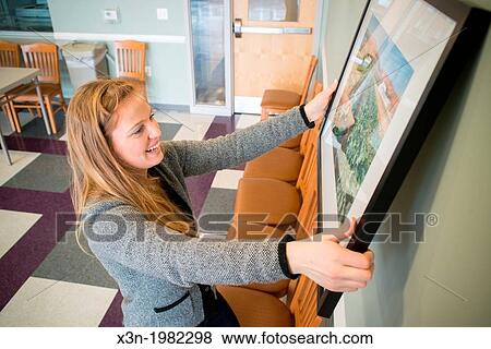 Young woman hanging photographs on wall. View Large Photo Image Stock Photo - Young woman hanging photographs on wall.. Fotosearch