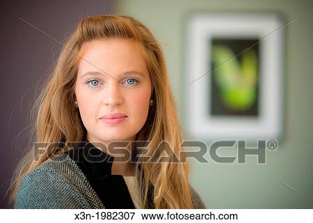 Stock Photo - Young woman hanging photographs on wall.. Fotosearch