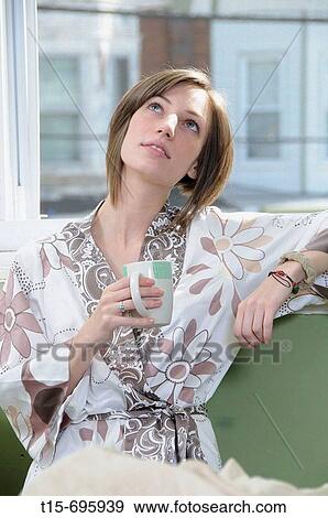 Stock Photo - Young woman having a cup of coffee by a window. Fotosearch