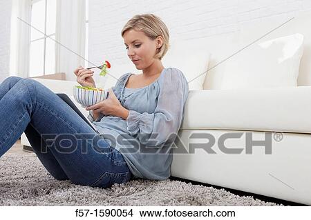 Picture - Young woman having lunch while socializing on her tablet computer. Fotosearch