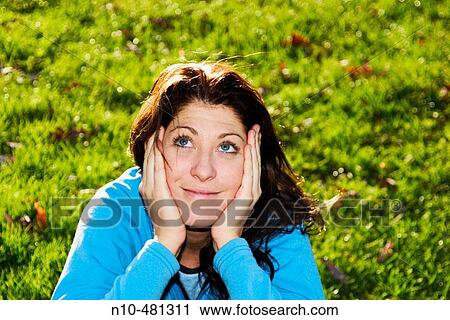 Young woman, her head resting in her hands, sitting on the grass at a park View Large Photo Image Stock Image - Young woman, her head resting in her hands, sitting on the grass at a park. Fotosearch