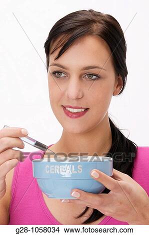 Picture - young woman holding a bowl of cereals and having breakfast. Fotosearch