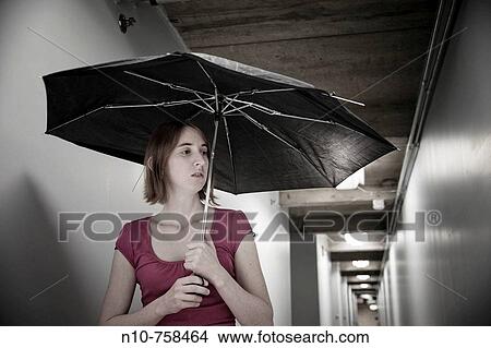 Young woman, holding a broken umbrella, standing in the basement hallway of an office building. View Large Photo Image Picture - Young woman, holding a broken umbrella, standing in the basement hallway of an office building.. Fotosearch