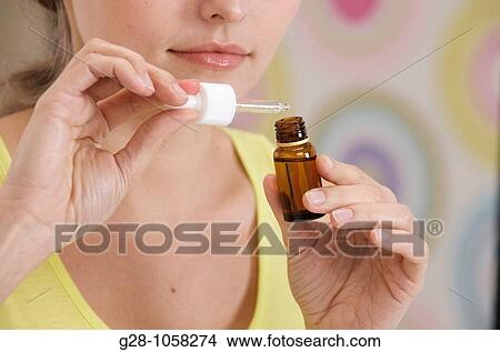 Picture - young woman holding a dropper and smelling a small bottle of essential oil. Fotosearch