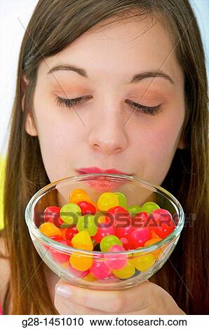 Stock Image - Young woman holding a glass jar full of colored sweets. Fotosearch