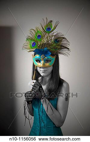 Stock Photograph - Young woman holding a mask over her face. Fotosearch