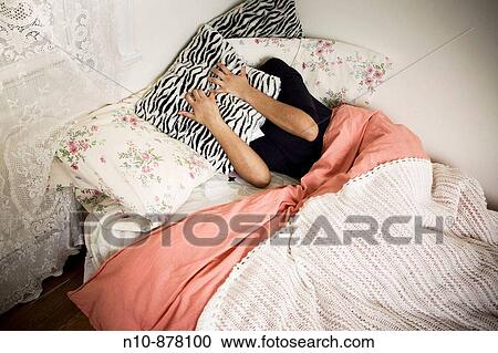 Stock Image - Young woman holding a pillow over her face.. Fotosearch