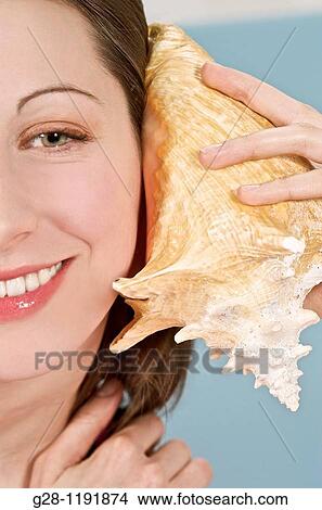 Young woman holding a shell to her ear to symbolize hearing problems View Large Photo Image Picture - Young woman holding a shell to her ear to symbolize hearing problems. Fotosearch