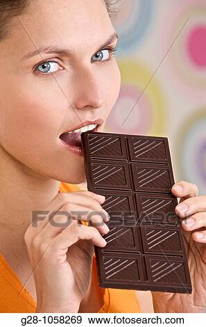 young woman holding a tablet of dark chocolate and biting it View Large Photo Image Stock Photo - young woman holding a tablet of dark chocolate and biting it. Fotosearch