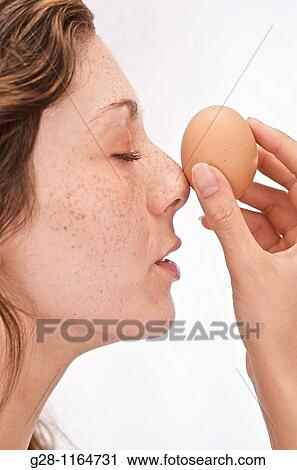 Stock Image - young woman holding an egg in front of her face, on her nose with closed eyes. Fotosearch
