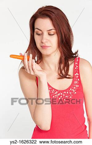 Stock Image - Young woman holding an organic carrot like a cigar. Fotosearch