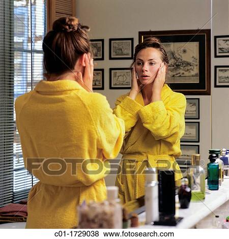 Stock Photo - young woman holding her face in front of bathroom mirror. Fotosearch