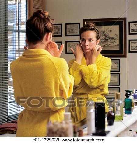 Stock Photo - young woman holding her face in front of bathroom mirror. Fotosearch