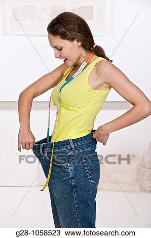 young woman holding her too large jeans after a slimming diet with measuring tape around her neck View Large Photo Image Stock Image - young woman holding her too large jeans after a slimming diet with measuring tape around her neck. Fotosearch