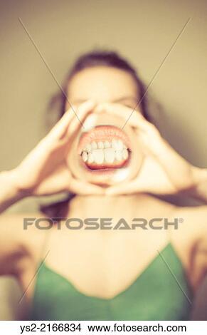 Young woman holding magnifying glass in front of mouth, showing her teeth. View Large Photo Image Picture - Young woman holding magnifying glass in front of mouth, showing her teeth.. Fotosearch