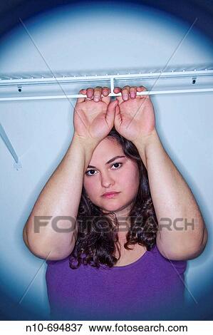 Stock Photo - Young woman holding the empty clothes rack inside a clothes closet. Fotosearch