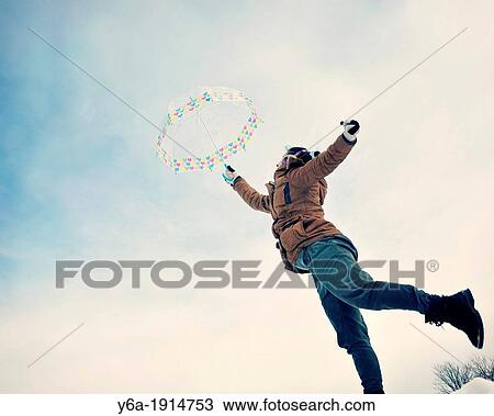 Stock Image - Young woman holding umbrella balancing on one leg. Fotosearch