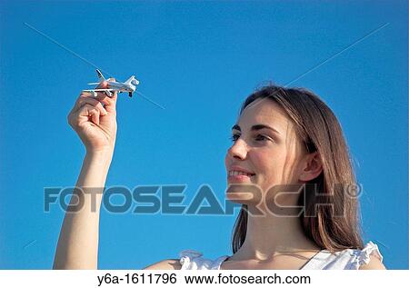 Young woman holding up toy airplane against blue sky View Large Photo Image Stock Photograph - Young woman holding up toy airplane against blue sky. Fotosearch