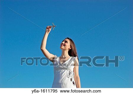 Young woman holding up toy airplane against blue sky View Large Photo Image Stock Photography - Young woman holding up toy airplane against blue sky. Fotosearch