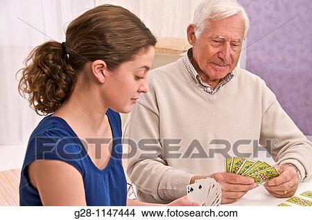 Young woman home help or grand daughter playing cards with senior man or grandfather View Large Photo Image Picture - Young woman home help or grand daughter playing cards with senior man or grandfather. Fotosearch