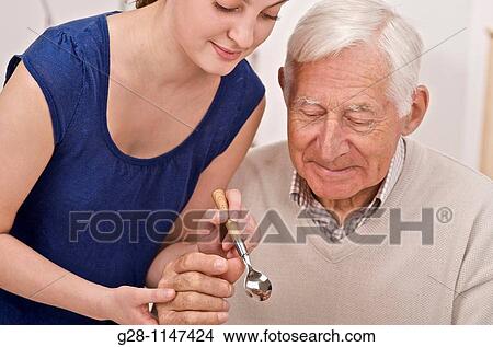 young woman, home help, or grand daughter helping a senior man or grandfather to hold a spoon to eat View Large Photo Image Picture - young woman, home help, or grand daughter helping a senior man or grandfather to hold a spoon to eat. Fotosearch