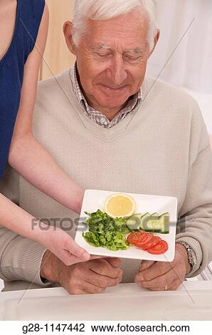 Young woman, home help or grand daughter serving his meal to a senior man or grandfather View Large Photo Image Stock Image - Young woman, home help or grand daughter serving his meal to a senior man or grandfather. Fotosearch