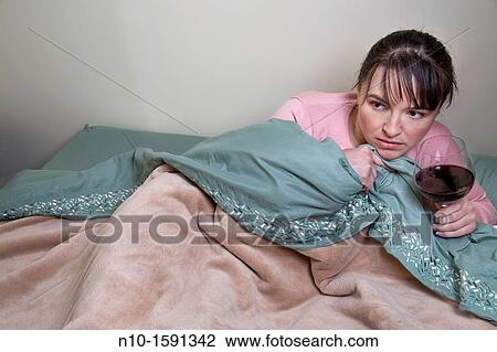 Stock Image - Young woman, in bed, holding a glass of wine. Fotosearch