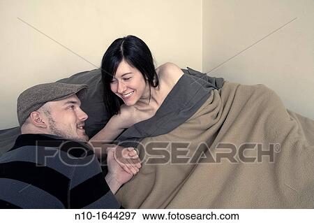 Stock Photo - Young woman in bed, holding her boyfriend's hand. Fotosearch