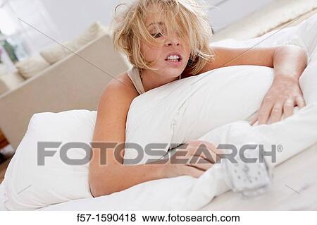 Stock Photo - Young woman in bed upset with her alarm clock. Fotosearch