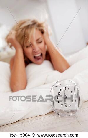 Young woman in bed upset with her alarm clock View Large Photo Image Stock Photo - Young woman in bed upset with her alarm clock. Fotosearch