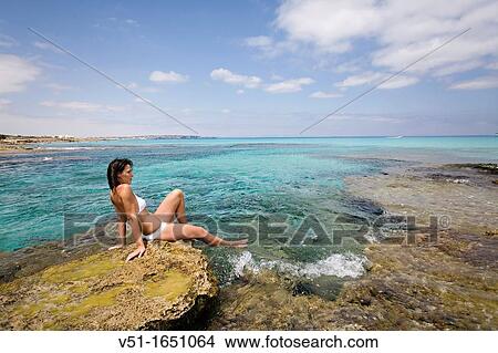 Young woman in bikini sitting on the rocks and enjoying the sea in Formentera, Spain View Large Photo Image Picture - Young woman in bikini sitting on the rocks and enjoying the sea in Formentera, Spain. Fotosearch