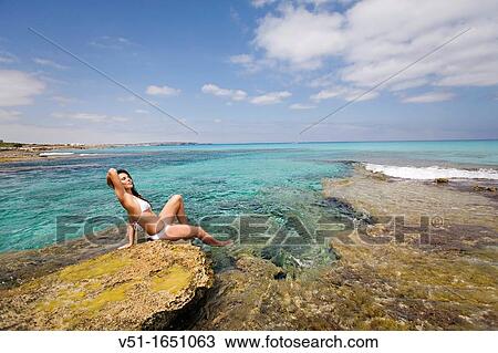 Young woman in bikini sitting on the rocks and enjoying the sea in Formentera, Spain View Large Photo Image Stock Image - Young woman in bikini sitting on the rocks and enjoying the sea in Formentera, Spain. Fotosearch