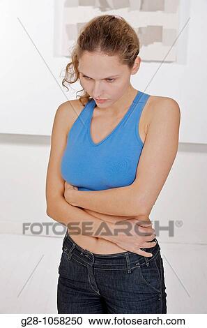 Stock Image - young woman in blue sports top holding her stomach with her hands suffering from periods or stomach pains. Fotosearch