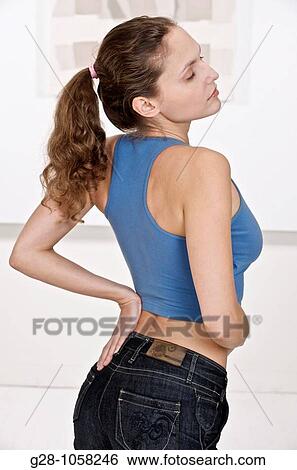 young woman in blue sports top, suffering from backache and holding her back with one hand View Large Photo Image Stock Photograph - young woman in blue sports top, suffering from backache and holding her back with one hand. Fotosearch