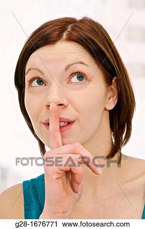 Stock Image - Young woman in blue with one finger on her lips. Fotosearch
