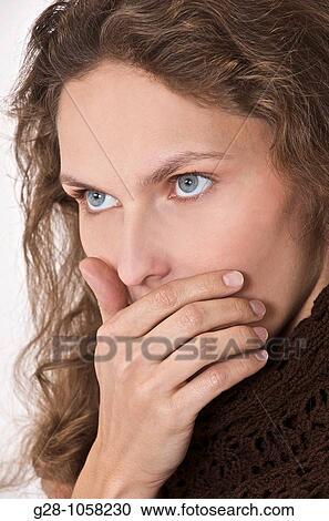 Stock Image - young woman in brown stopping her mouth with her hand, too shy to express herself, or regretting her words. Fotosearch