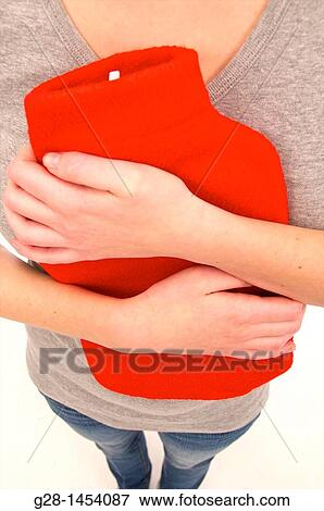 Stock Photo - Young woman in grey, head invisible, holding a red hot water bottle on her painful stomach. Fotosearch