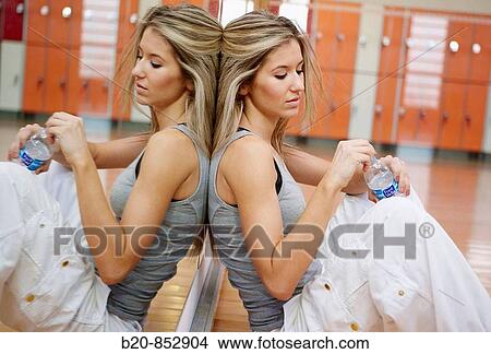 Picture - Young woman in gym resting and drinking water. Fotosearch