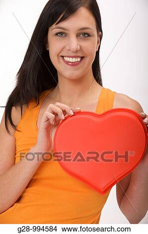 young woman in orange holding a red heart in front of her for love or heart problems View Large Photo Image Picture - young woman in orange holding a red heart in front of her for love or heart problems. Fotosearch