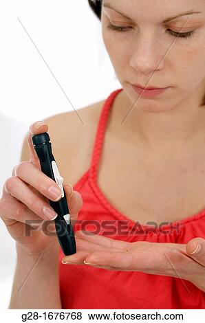 Stock Photo - Young woman in red, pricking her finger to analyse rate of glucose sugar in her blood for diabetes. Fotosearch