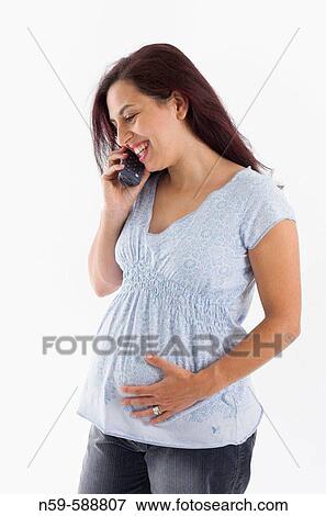 Stock Photo - Young woman in the early stages of pregnancy shares her exciting news on the telephone. Fotosearch