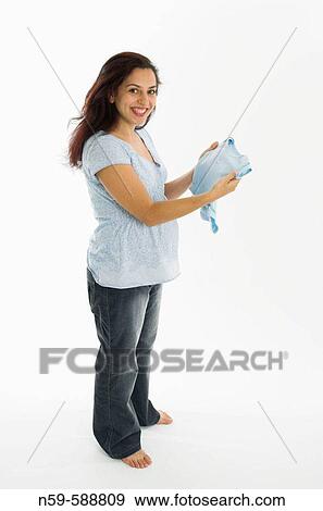 Stock Photo - Young woman in the early stages of pregnancy looking at baby clothes.. Fotosearch