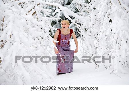 Stock Image - Young Woman in Wedding Dress Looking Through Snowy Branches. Fotosearch