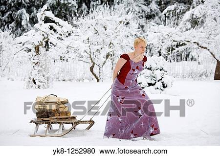 Stock Image - Young Woman in Wedding Dress Pulling Wooden Sledge with Firewoods. Fotosearch
