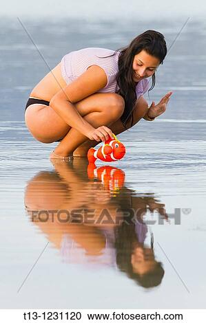 Stock Image - Young woman is placing a small toy fish on a water. Fotosearch