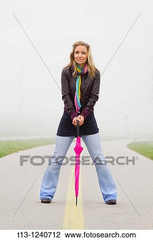 Stock Image - Young woman is posing with a closed pink umbrella. Fotosearch