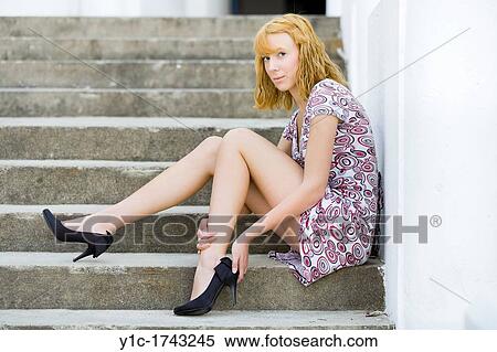 Stock Photography - Young woman is removing her high-heeled shoe. Fotosearch